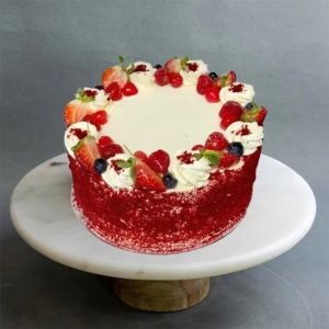 A Red Velvet Cake with swirls of cream and red berries on top