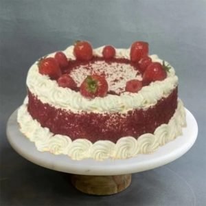 A Red Velvet Cake with swirls of cream and strawberries on top
