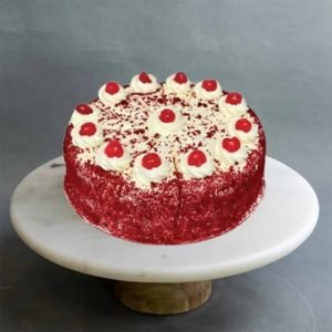 A Red Velvet Cake with swirls of cream and cherries on top